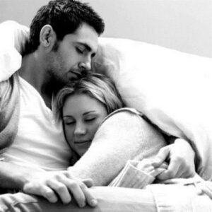 A couple in the bed. She puts her head on his chest to feel his heartbeat.